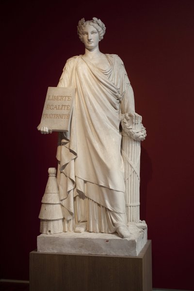 La República Francesa. Representada como una mujer vestida con un manto antiguo y sosteniendo una placa con el lema "Libertad, Igualdad, Fraternidad", la colmena a sus pies representa fertilidad y orden, el hacha y la viga son insignias de poder, esta aleg de Ferdinand Taluet
