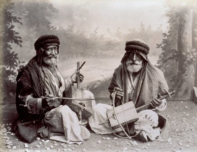 Retrato de dos músicos árabes con vestimenta étnica humilde. Los hombres mayores están posando en el estudio, sentados en el suelo. Detrás de ellos hay un fondo de un paisaje boscoso de Félix Bonfils