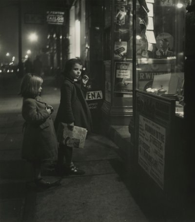 Dos niñas con abrigos de invierno en la puerta de una tienda por la noche de Godfrey Macdominic