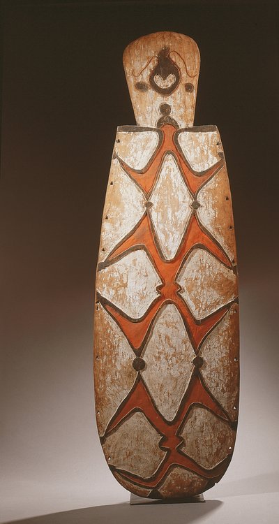 Escudo ovalado Asmat, tallado en relieve con figuras estilizadas, una máscara en la parte superior de Guinean New