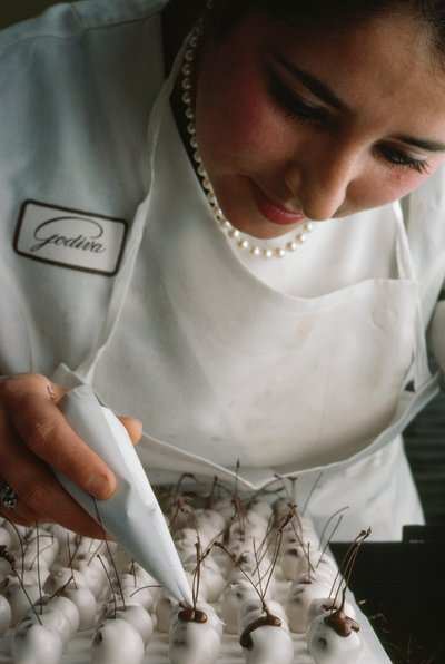 Un chef de Godiva fija tallos de chocolate a cerezas cubiertas de fondant. Bruselas, Bélgica. de James L Stanfield