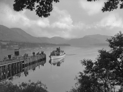 Un barco que transporta personas en un lago se acerca a un embarcadero, las colinas al fondo de Joseph Hardman