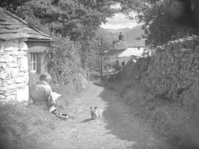 Una mujer sentada leyendo con un perro en un callejón de Joseph Hardman