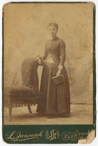 Fotografía de una mujer de pie junto a una silla y sosteniendo un libro, finales del siglo XIX de Louis Janousek