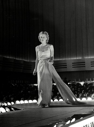 Modelo fotografiada en una pasarela con vestido de noche con tirantes de pedrería; el artículo es una creación de la casa de alta costura "Fumach". de Luis Bogino
