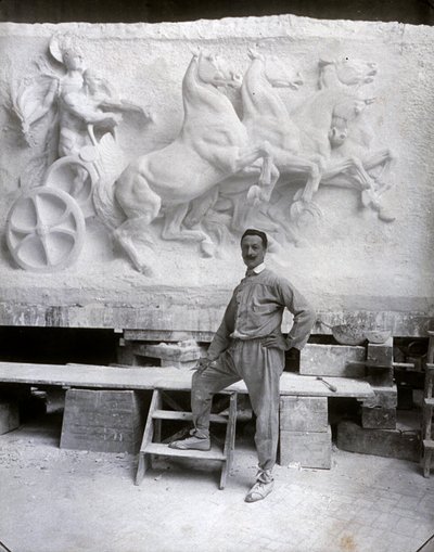 Retrato de cuerpo entero del famoso escultor Pietro Canonica. Está posando en su estudio frente a un alto relieve de mármol en el que está trabajando de Mario Nunes Vais