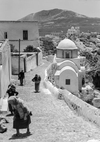 Aldeanos griegos caminan por una calle empedrada en un pueblo griego con... de Maynard Owen Williams