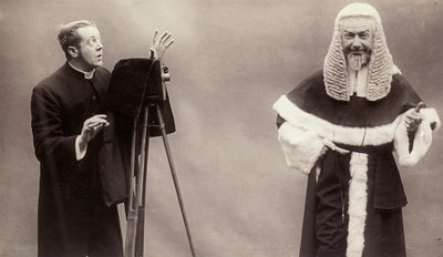 Un hombre con sotana apunta la lente de su cámara a un hombre vestido como un papa de Rotary Photographic Co Ltd