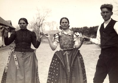 Dos damas y un hombre, vestidos con trajes tradicionales húngaros, bailan cogidos de la mano, con unas velas en las manos de Rudolf Balogh