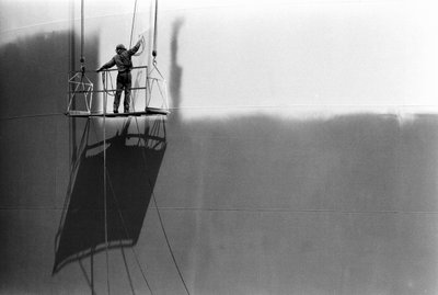 Hombre en una plataforma pintando un tanque de almacenamiento de petróleo. de Ted Spiegel