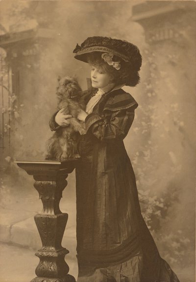 [Sarah Bernhardt de pie en un estudio, sosteniendo un perrito negro sobre un pedestal de madera tallada y ornamentada] de Theodore C. Marceau