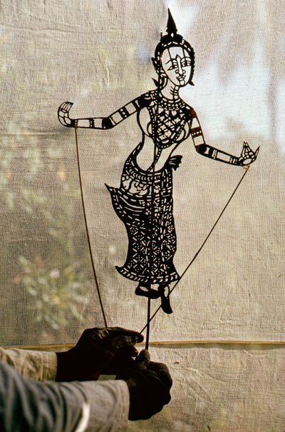 Un titiritero manipula una marioneta de sombras argumentales contra un telón para una obra de sombras. C... de Thomas J. Abercrombie