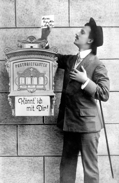 Un hombre elegante con traje, sombrero y bastón, publica una nota en un buzón. Alemania alrededor de 1920 de Unbekannt