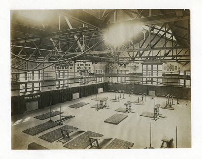 Fotografía horizontal del interior de un gran gimnasio. Equipos y colchonetas están esparcidos por el suelo de Unbekannt