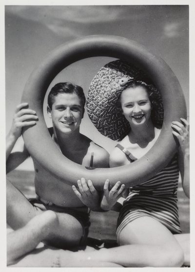 Hombre y mujer mirando a través de un aro de goma en la playa, c 1935 de Unbekannt