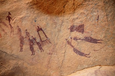 Arte rupestre, Prehistoria: Pintura rupestre de un grupo de personajes y "guerbas" (odres) con y sin flecos en un refugio ornamentado, en el macizo de Uweinat, Sudán. Período de 8000 a 3000 años a.C. Fotografía de Unbekannt