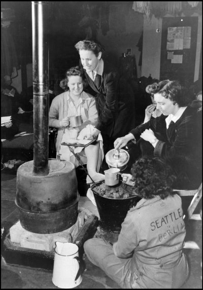 Segunda Guerra Mundial (1939-1945): en una base aérea británica donde una unidad del WAC (Cuerpo de Ejército de Mujeres) está confinada, un grupo de ellas toma un refrigerio alrededor de la estufa de su habitación. Fotografía 1943. de Unbekannt