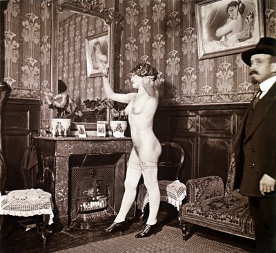 Enigmática fotografía que muestra a una joven completamente desnuda (salvo los zapatos y las medias) peinándose ante un espejo en presencia de un hombre vestido y calentado con un sombrero. Podría pensarse que se trata de una foto tomada en un burdel, pero de Unbekannter Künstler