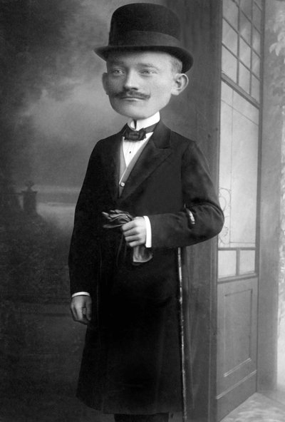 Retrato de un hombre muy elegante con cabeza de gigante, lleva sombrero de melón, bastón, pajarita y abrigo negro. Se trata de un fotomontaje. Annees 1910 Fotografía histórica, hombre con cabeza de gigante de Unbekannter Künstler