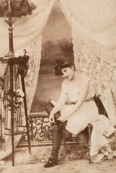 Retrato de una joven en ropa íntima, sentada mientras se ata los cordones de los zapatos. de Unknown photographer