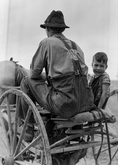 Un granjero y un niño sonriente montan en el asiento de una calesa tirada por caballos en Virginia Occidental de Volkmar Wentzel