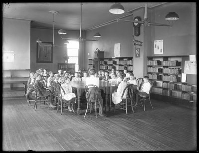 Niños escuchan a una mujer en la sala de lectura de una sucursal no identificada de la Biblioteca Pública del Borough de Queens, c.1910 de William Davis Hassler