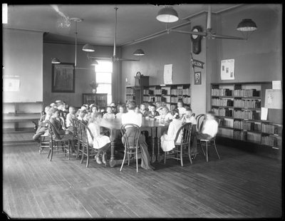 Niños escuchan a una mujer en la sala de lectura de una sucursal no identificada de la Biblioteca Pública del Borough de Queens, c.1910 (foto en blanco y negro) de William Davis Hassler
