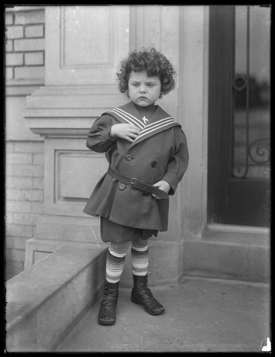 Niño pequeño con traje de marinero en la entrada del edificio de apartamentos de la Avenida Vermilyea, c.1913 de William Davis Hassler