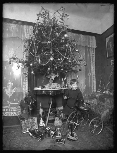 Niño Seymour posando con triciclo junto al árbol de Navidad en el salón, Navidad 1912 de William Davis Hassler