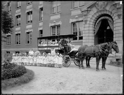 Niñas pequeñas posan dentro y frente a un carro tirado por caballos, frente a un edificio no identificado, probablemente el Asilo de Huérfanos Católicos Romanos, Kingsbridge, Bronx, c.1910 de William Davis Hassler