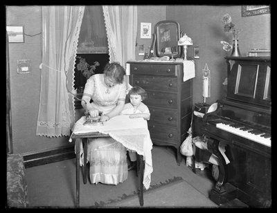 Mujer no identificada demostrando el uso de una plancha eléctrica, observada por una niña pequeña de William Davis Hassler