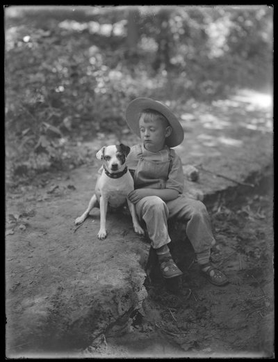 William Gray Hassler con sombrero de paja y overoles, posando sentado en el bosque con un perro pequeño (Bessie), 20 de agosto de 1911 de William Davis Hassler