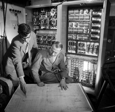 Ingenieros discuten planes frente al panel de control electrónico que han construido de Frederick (attr. to) Barnard