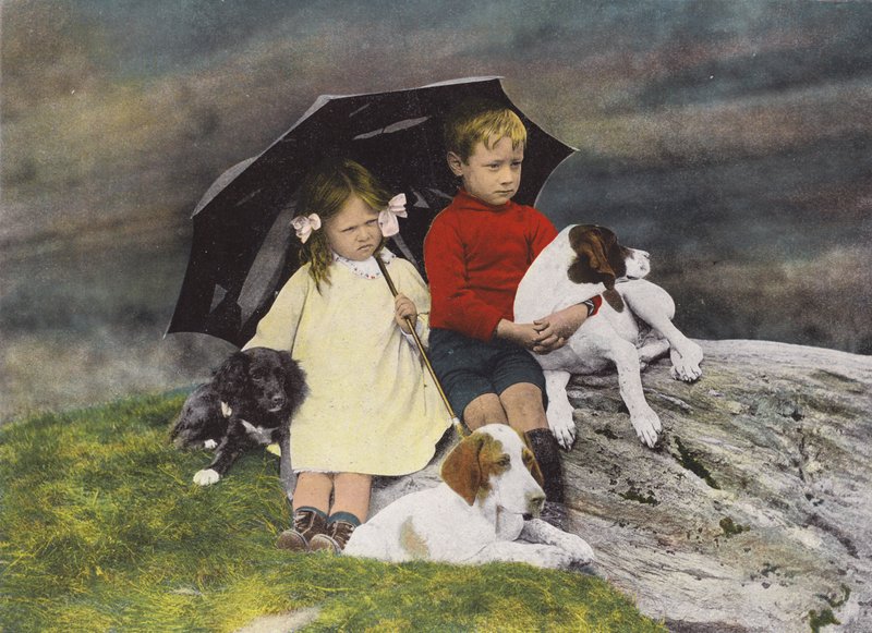 Niño y niña con tres perros cobijados bajo un paraguas (foto coloreada) de English Photographer