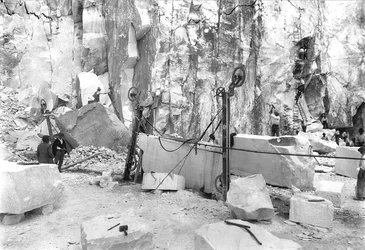 Excavadores trabajando en una cantera de mármol en los Alpes Apuanos, Toscana. En primer plano hay bloques de mármol ya cuadrados.