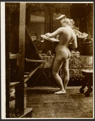 [Modelo desnuda de pie en un estudio con un cuaderno de dibujo en la mano].