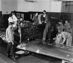 Soldados en formación trabajan en «Flying Patch», un avión de combate Curtiss «Warhawk» sin motor ni conjunto de cola, con agujeros de bala simulados y parches, hacia 1942