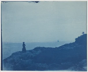 Mujer observando goleta desde un promontorio rocoso