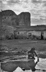 Niña jugando con un barco de papel en un charco rodeado de barro, Venosa, Basilicata, Italia