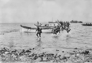 Soldados australianos vadeando el agua al desembarcar en Anzac Cove, Gallipoli el 25 de abril de 1915 después de ser transportados en botes de desembarco desde barcos más grandes en el fondo, 25 de abril de 1915