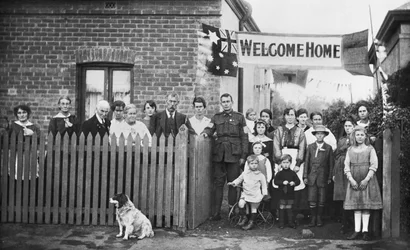 Retrato de grupo del 540 Zapador Arthur Findon Dunbar MM, 2ª Compañía de Túneles Australiana (con uniforme y su brazo apoyado en la puerta) y sus familiares reunidos fuera de su casa en 45 Chief Street