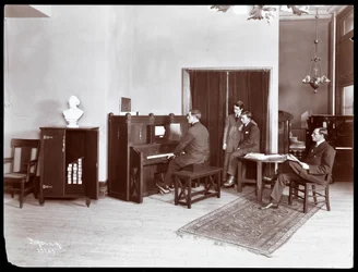 Cuatro hombres, uno tocando un piano de la compañía H. Bruman Co., 1907