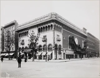 Un enorme teatro con una fachada elaborada, con arcos moriscos y balcones. Un gran letrero en lo alto del edificio dice „B.S. Moss Regent Theatre Vaudeville & Feature Films“. Un letrero que anuncia a Olga Petrova en „The Heart of a Painted Woman“ cuelga
