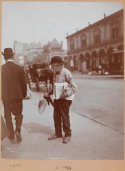 Un hombre de pie en la acera de Broadway entre la calle 34 y la calle 35 sosteniendo el periódico The Evening Telegram