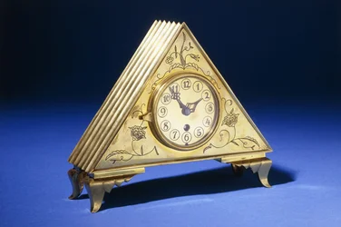 Un reloj de mesa triangular de latón con decoración floral grabada