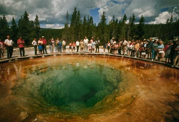 Los visitantes del parque se reúnen alrededor de una poza termal verde azulada con forma de flor. Parque Nacional de Yellowstone