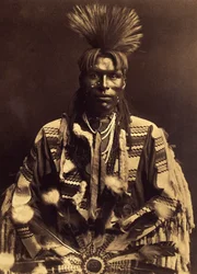 Un dandy piegan. Hacia 1855, los jóvenes empezaron a hacerse una raya en el pelo de una sien a la otra y a rizarse la espalda con la varita de un fusil precalentado. Algunos se hacían nates, otros no. Foto tomada del volumen 6 de la enciclopedia publicada