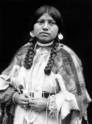 Mujer Cayuse, retrato de medio cuerpo, de pie, mirando al frente, trenzas, pendientes de disco de concha, gargantilla de cuentas de concha y cuentas de concha alrededor del cuello, vestido de piel de ante con cuentas y cinturón de cuentas c. 1910, foto Edw