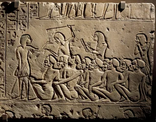 Un grupo de prisioneros negroides rodeados por guardias armados con garrotes mientras un escriba redacta un informe, relieve de la tumba de Horemheb en Saqqara.