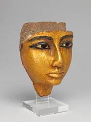 Rostro de un ataúd, con ojos y cejas incrustados, dorado